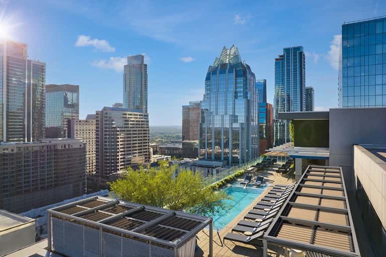Rooftop pool and lounge area with city skyline views, featuring sunbeds and modern high-rise buildings