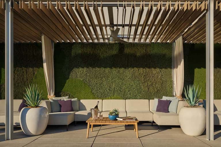Luxurious pergola-shaded seating area with cream sectional sofa, potted plants, and green living wall backdrop