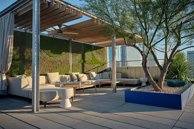 Contemporary rooftop lounge with wooden pergola, cream seating, live tree, and city skyline in background