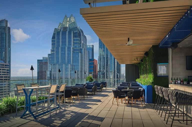 Elevated outdoor bar and lounge with city views, glass railings, and distinctive architectural tower visible