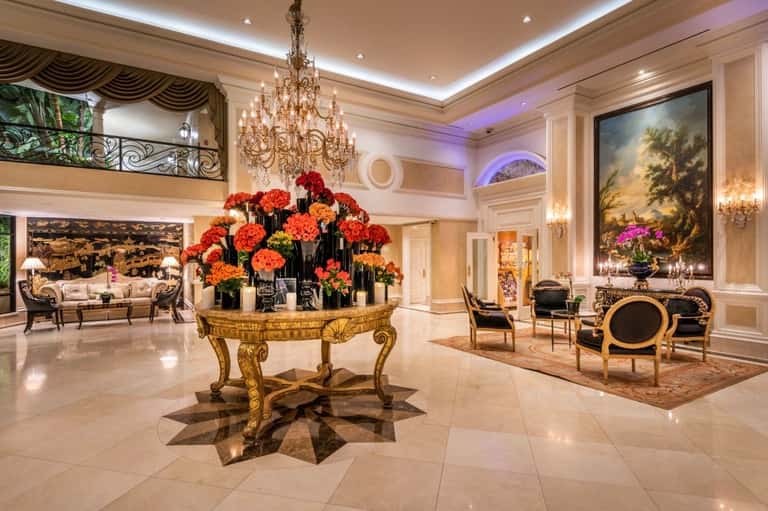 Luxurious hotel lobby with marble floors, ornate golden centerpiece table with red flowers, crystal chandelier, and elegant seating areas