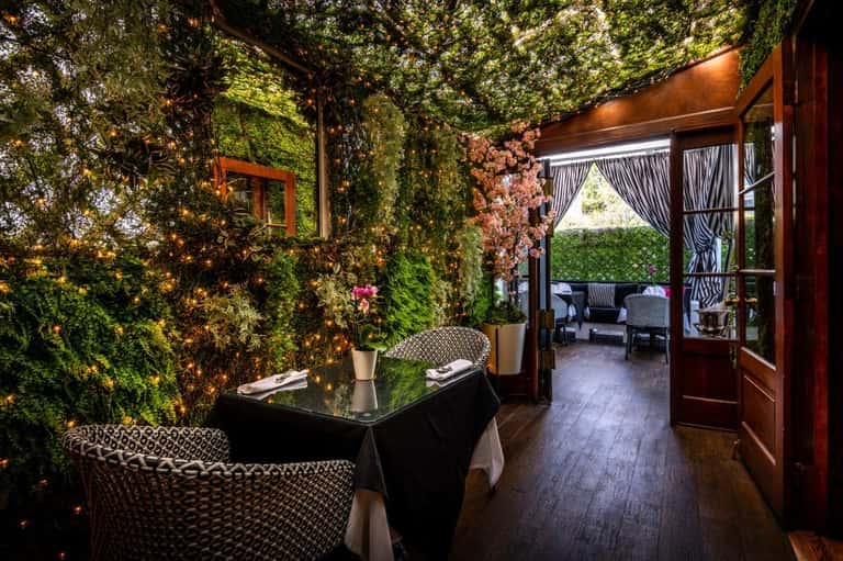 Indoor event space with living green walls, dark furniture, and open doors leading to an outdoor patio area