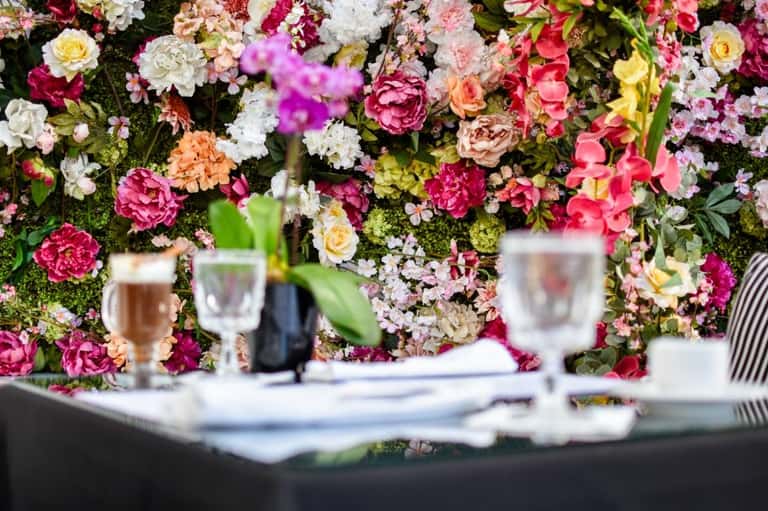 Colorful floral wall backdrop with dining table setting, wine glasses, and place settings in foreground