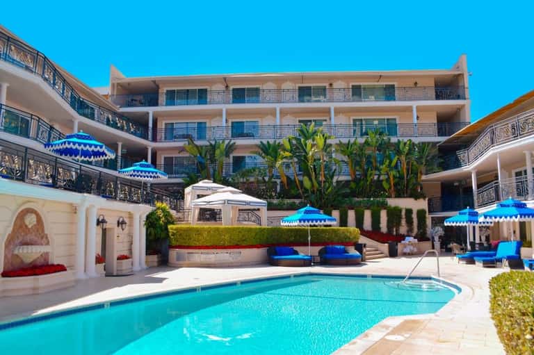 Luxury resort courtyard with turquoise pool, blue umbrellas, white lounge chairs, and ornate wrought iron railings