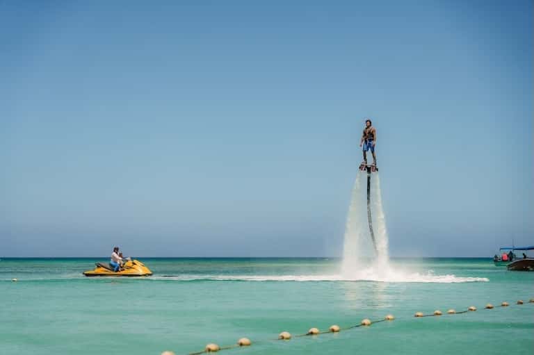 Man performing flyboarding over turquoise ocean water with jet ski support