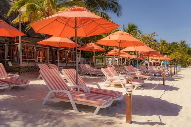 Beach lounge area with red and white striped chairs and large orange umbrellas