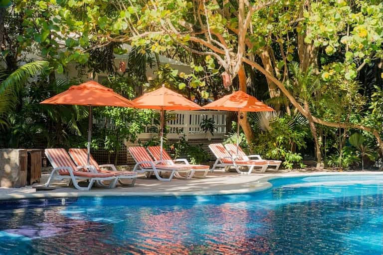Resort pool with orange umbrellas, striped lounge chairs, and dense tropical greenery