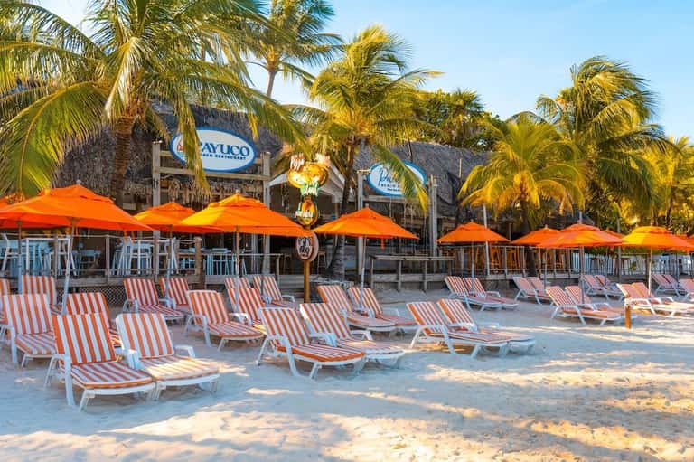 Beach resort with orange umbrellas, striped lounge chairs, and thatched-roof buildings