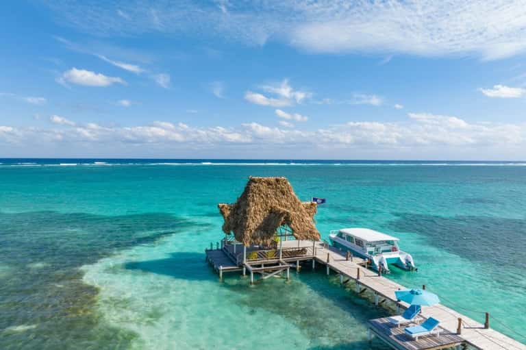 Aerial view of thatched-roof beach bar on wooden dock in crystal clear turquoise water