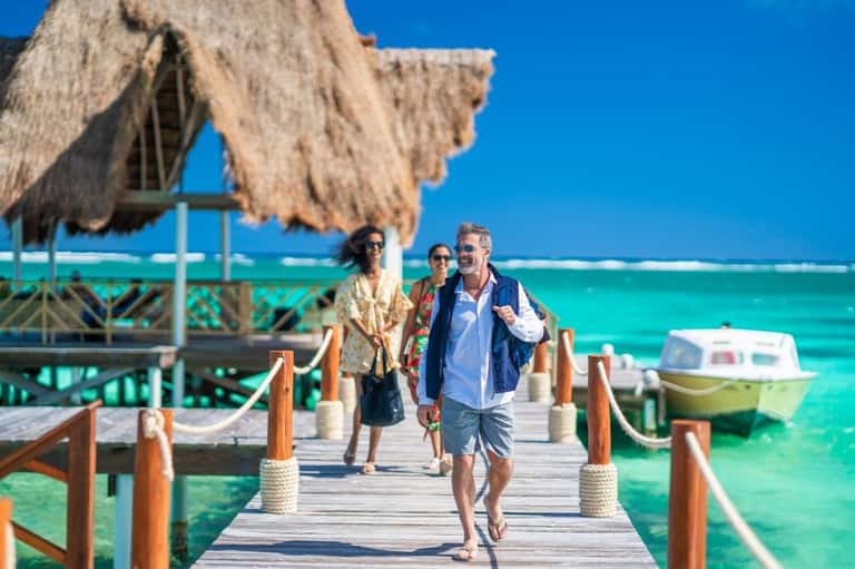Guests walking on wooden dock toward thatched beach cabana overlooking turquoise ocean