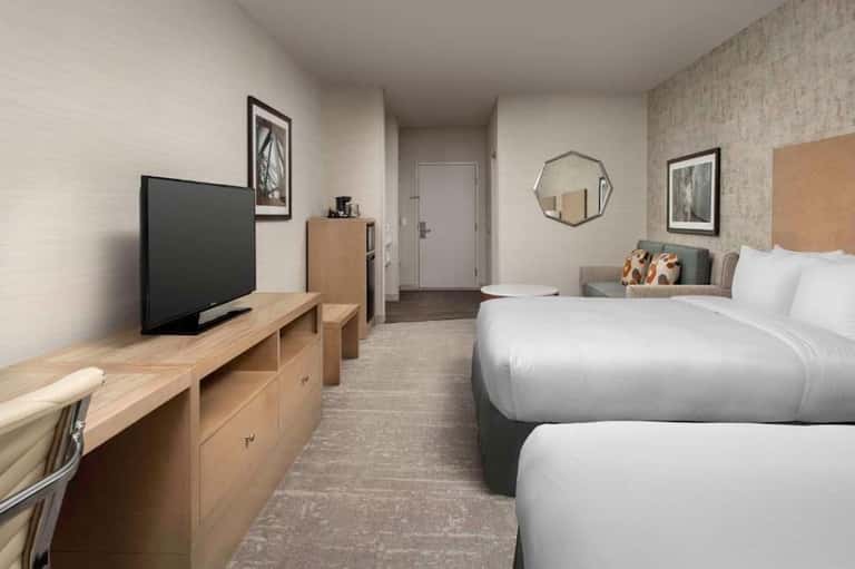 Hotel room with two queen beds, TV, wooden furniture, and modern bathroom