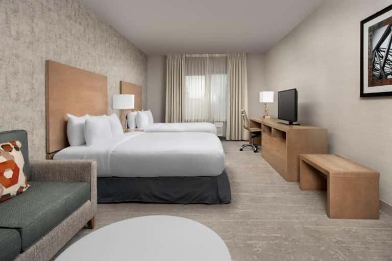 Modern hotel room with two queen beds, wooden furniture, and neutral decor