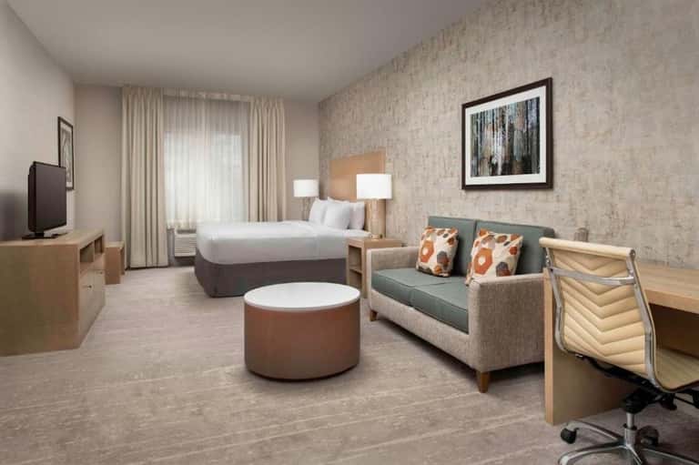 Spacious hotel suite with king bed, seating area, desk, and patio access