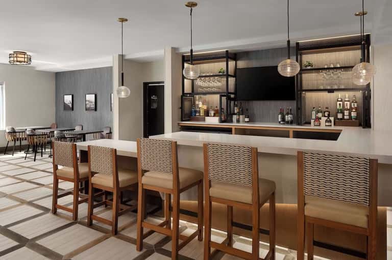 Hotel bar with wood accents, pendant lighting, and bar seating with patterned chairs
