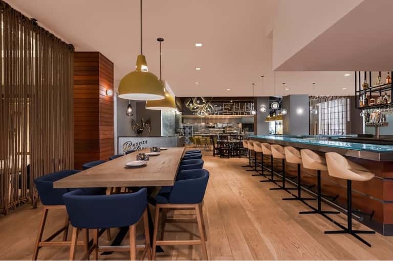 Hotel lounge with dining table, bar counter, and modern furnishings in warm tones