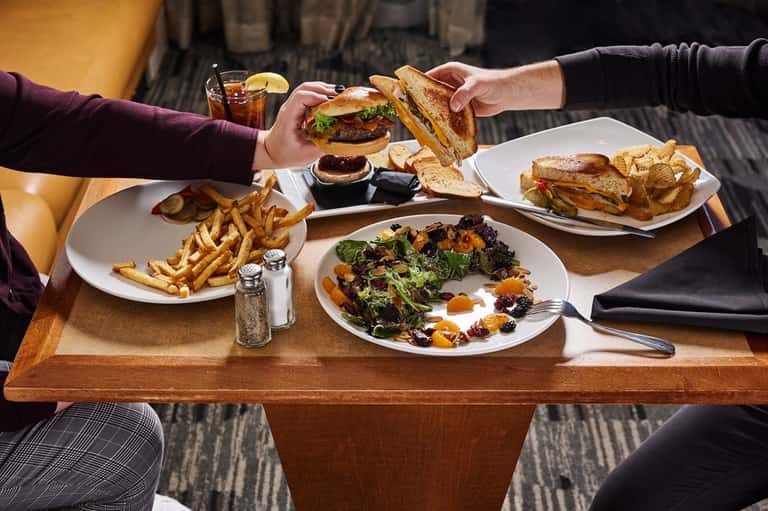 Two diners sharing burgers and fries at a casual restaurant table with cocktails
