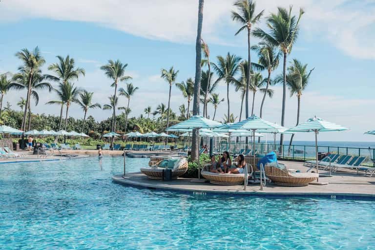 Resort pool with turquoise water, floating lounges, palm trees, and ocean view