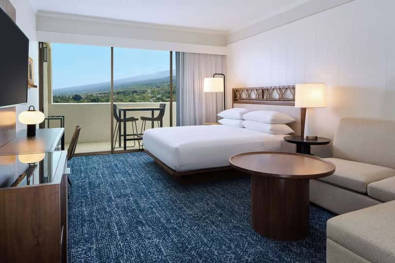 Upscale hotel room with ocean view balcony, white bed, and mountain landscape