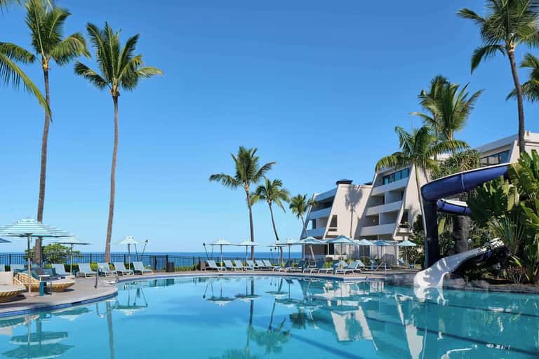 Oceanfront resort pool with turquoise water, palm trees, white loungers, and coastal hotel building