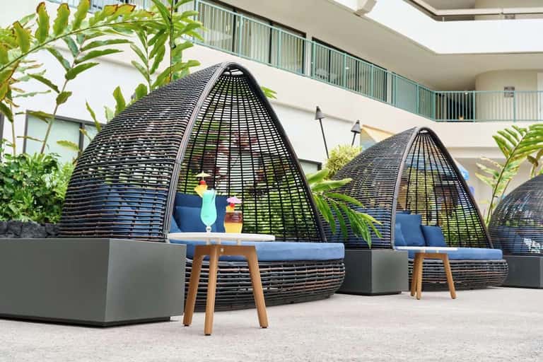 Resort courtyard with black woven egg-shaped lounge chairs on white stone patio near modern building