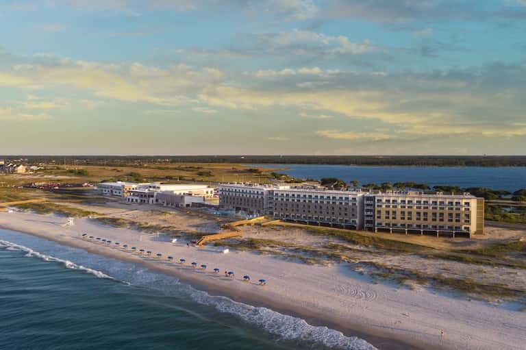 Beachfront resort aerial view showing buildings along sandy shore and bay landscape
