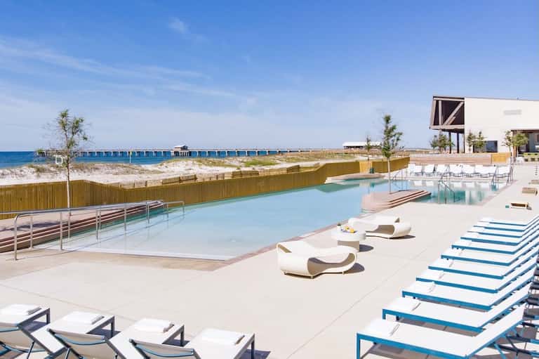 Modern beachfront pool deck with lounge chairs and ocean view, wooden fence barrier visible
