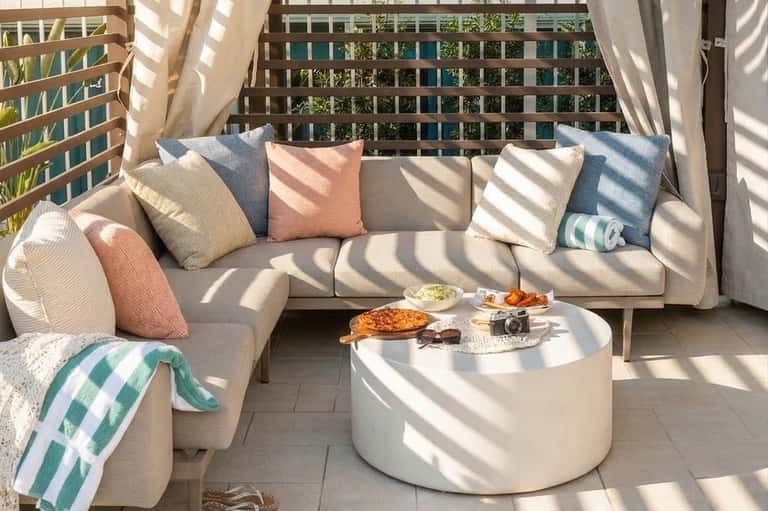 Coastal balcony seating area with cream sectional sofa, colorful pillows, white round coffee table, and striped beach towel