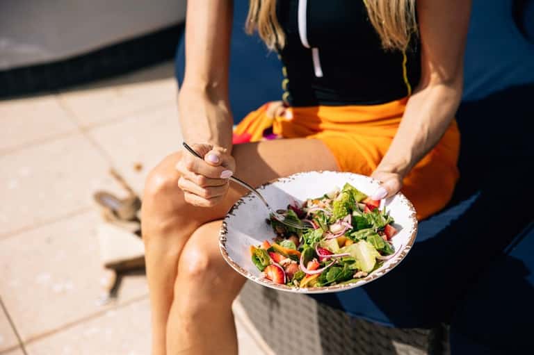 Person holding colorful fresh garden salad while seated poolside in summery attire