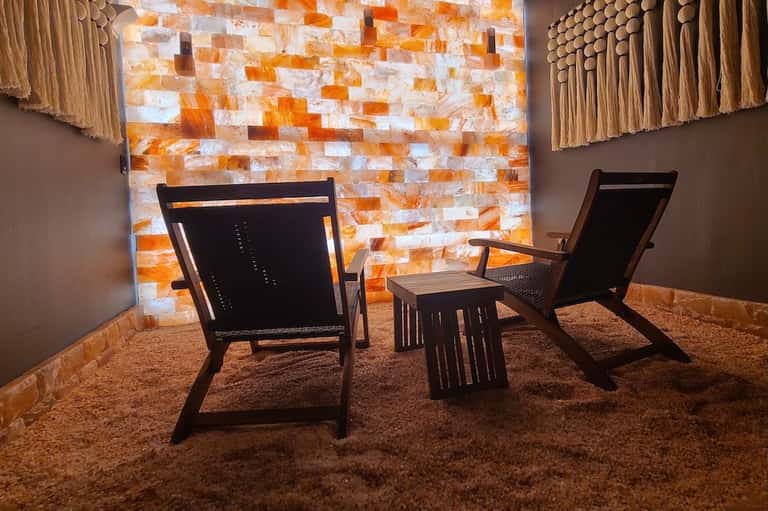 Salt therapy room with Himalayan salt brick wall and black wooden lounge chairs