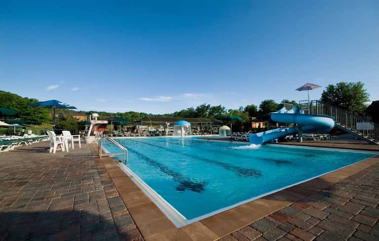 Outdoor swimming pool with blue water slide, white lounge chairs, and umbrella with scenic grounds