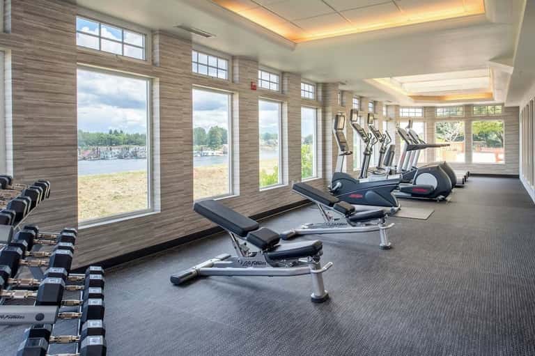 Indoor fitness center with cardio machines, dumbbells, and large windows overlooking waterfront