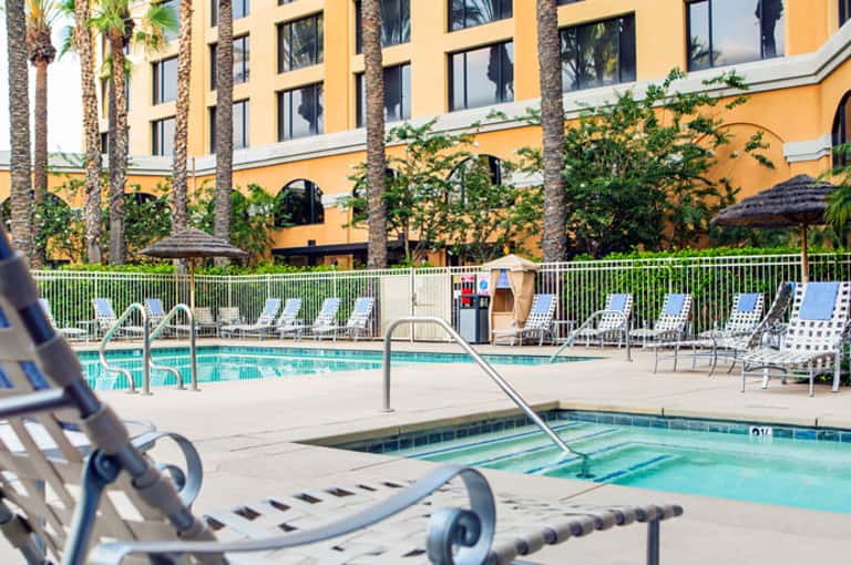 Yellow hotel building with palm trees and rectangular pool surrounded by white lounge chairs