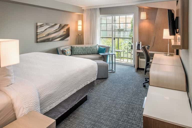 Spacious hotel room with king bed, comfortable seating area, balcony doors, and modern décor