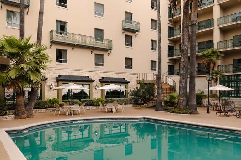 Hotel courtyard pool with multi-story building, palm trees, and dining area