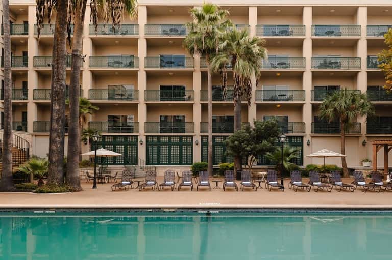 Beachfront resort pool with multi-story hotel tower and palm tree landscaping