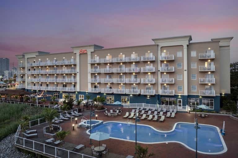 Waterfront hotel at dusk with illuminated building and curved pool with lounge seating