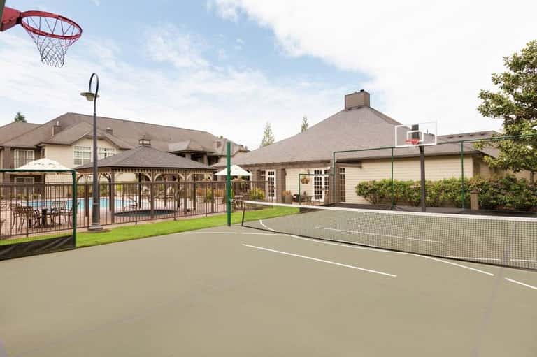 Outdoor sports court with basketball hoop and tennis net, adjacent to residential buildings