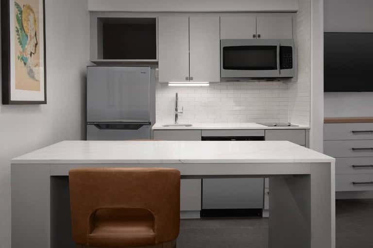 Modern kitchenette with white cabinetry, stainless steel appliances, and island seating with brown chair