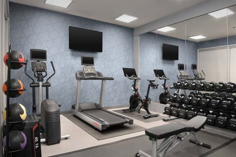 Fitness center with cardio equipment, dumbbells, treadmill, stationary bike, and patterned wall
