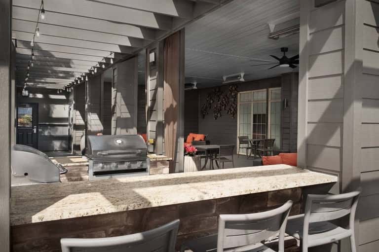 Covered outdoor entertaining space with bar seating, grill, pergola, and lounge area