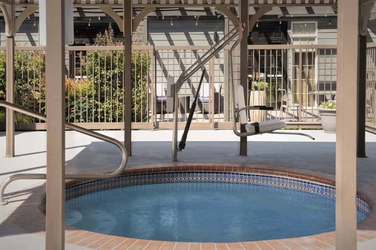 Circular hot tub under wooden pergola with loungers and landscaping visible beyond