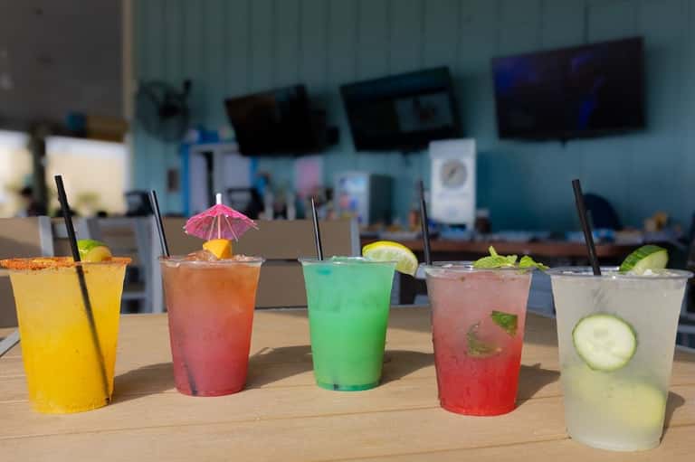 Five colorful tropical cocktails with umbrellas and lime garnishes on wooden table