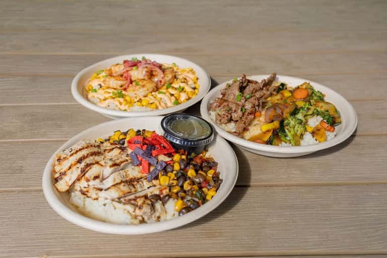 Three plated dishes featuring grilled proteins, roasted vegetables, and rice on wooden surface