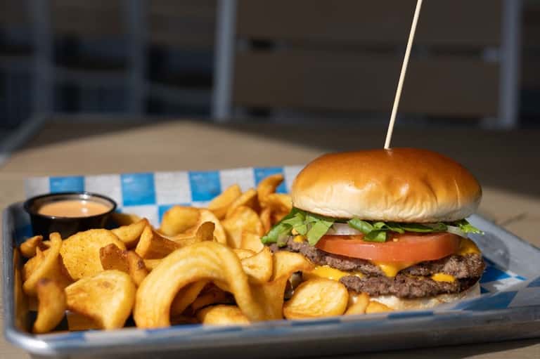 Gourmet burger with cheese and tomato served with waffle fries and sauce on checkered paper