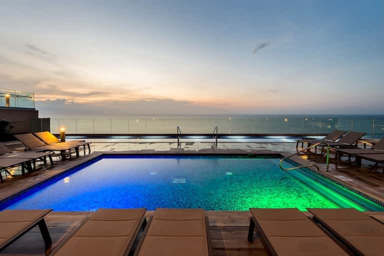 Rooftop infinity pool illuminated at dusk with ocean view and lounge chairs