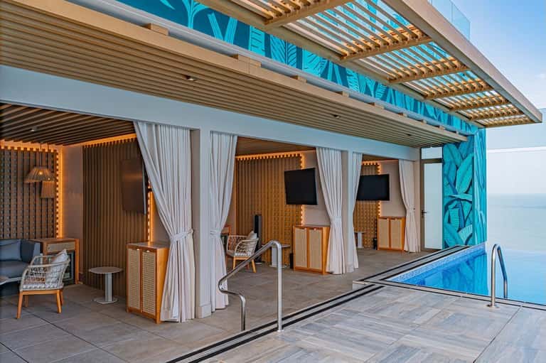 Poolside lounge area with wooden pergola, white curtains, and ocean views