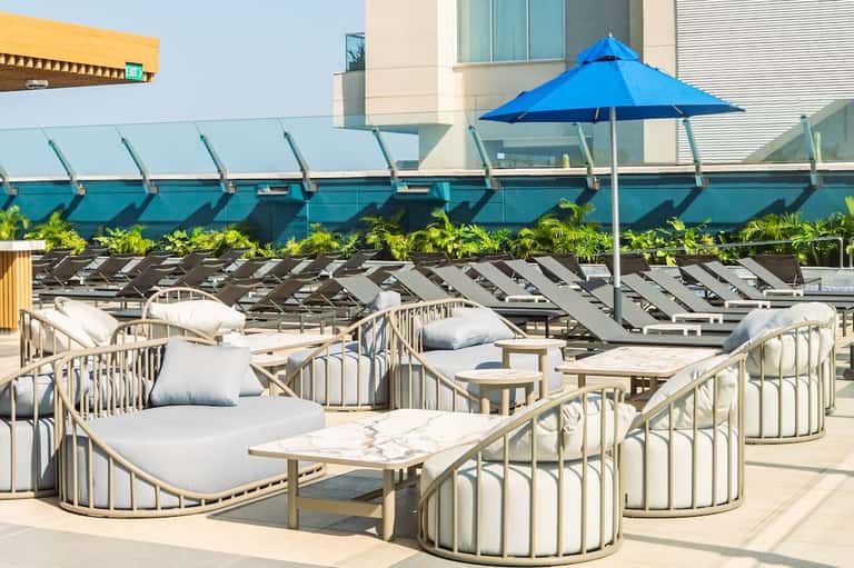Rooftop lounge area with curved seating pods, white cushions, blue umbrella, and city views