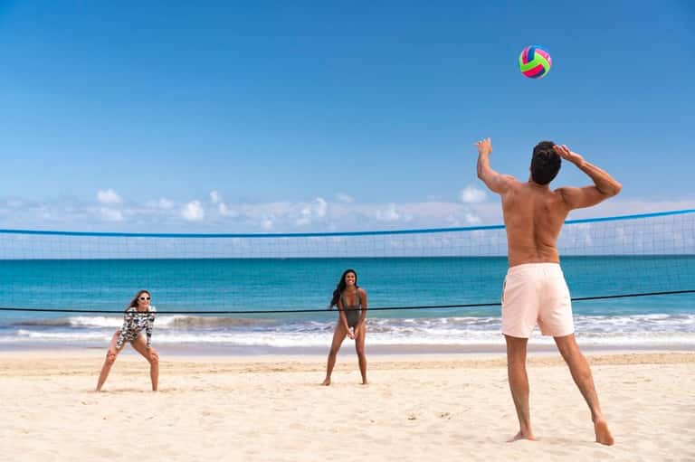 Group playing beach volleyball with net on sandy shore and ocean beyond