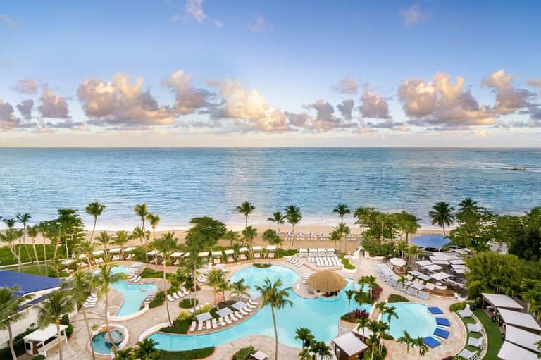 Aerial view of beachfront resort with multiple pools, palm trees, and turquoise ocean