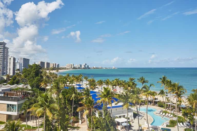 Beachfront resort aerial view showing pools, palm trees, and high-rise hotels along coast